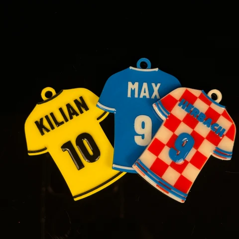 Foto von drei gedruckten Trikot-Schlüsselanhängern in Gelb, Blau und Rot-Weiß mit individuellen Namen und Nummern